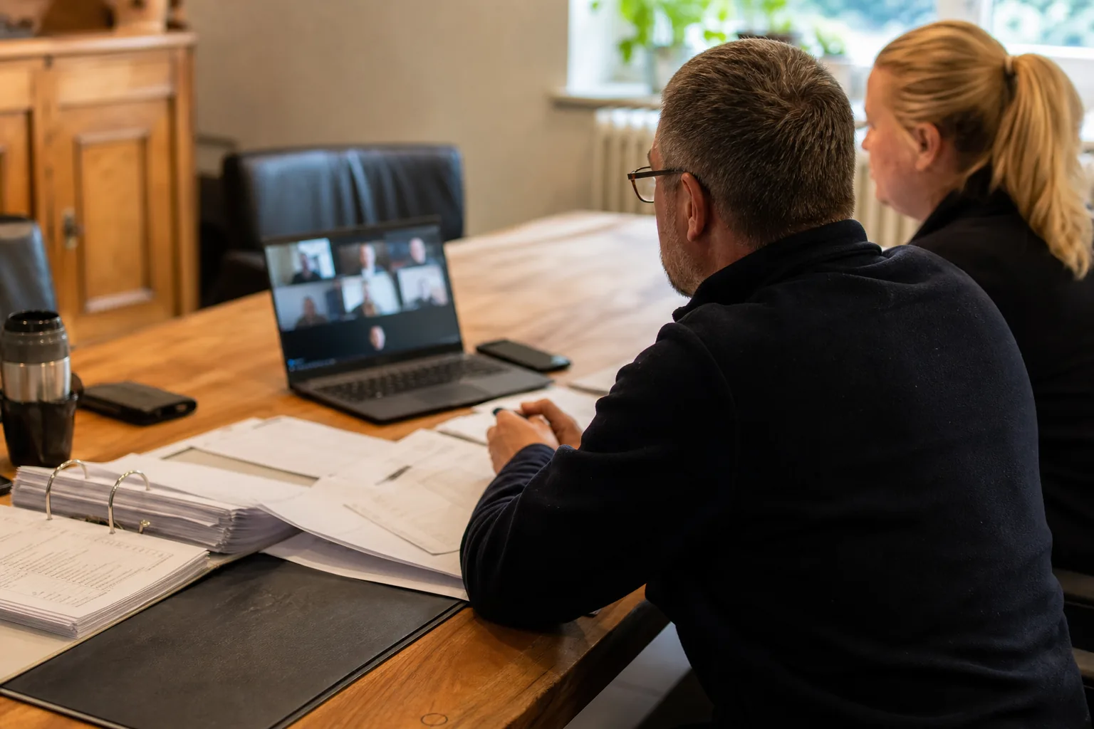 Eigentümer nehmen an einer Videokonferenz mit Versammlungsunterlagen auf einem Tisch teil.